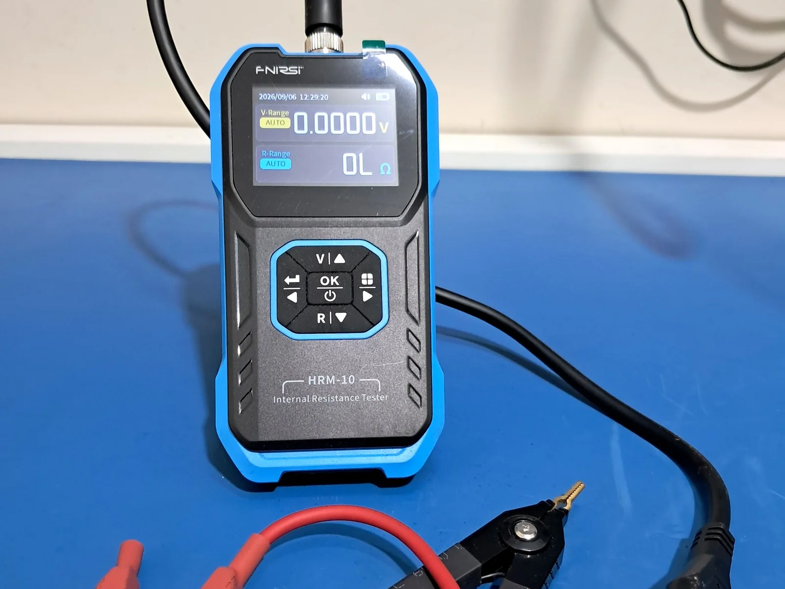 Testador de resistência interna FNIRSI HRM-10 sobre a bancada do laboratório da Keleuthos, com as garras de teste conectadas